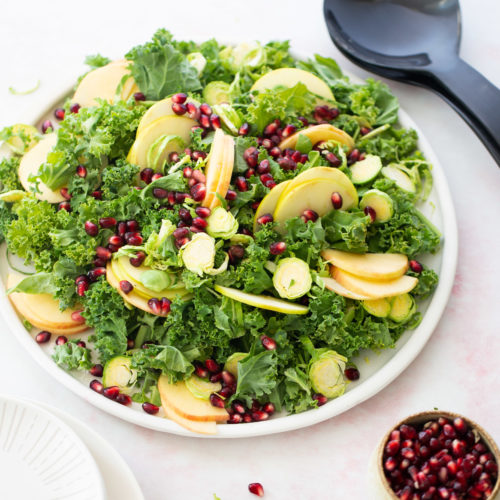 A plate of kale salad with apples and pomegranate.