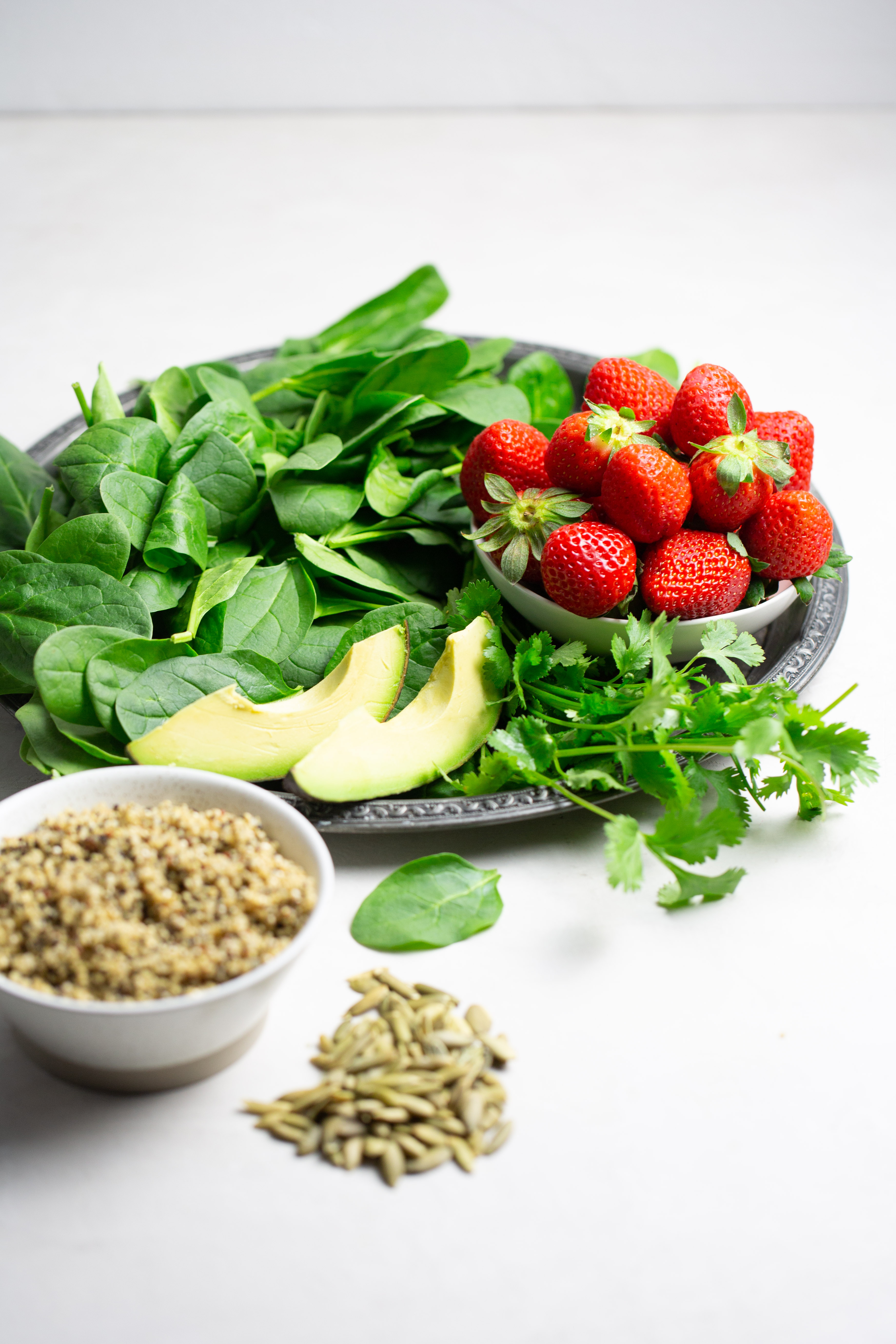 Plstter with spinach, strawberries, avocado and cilantro. A bowl of cooked quinoa on the side.