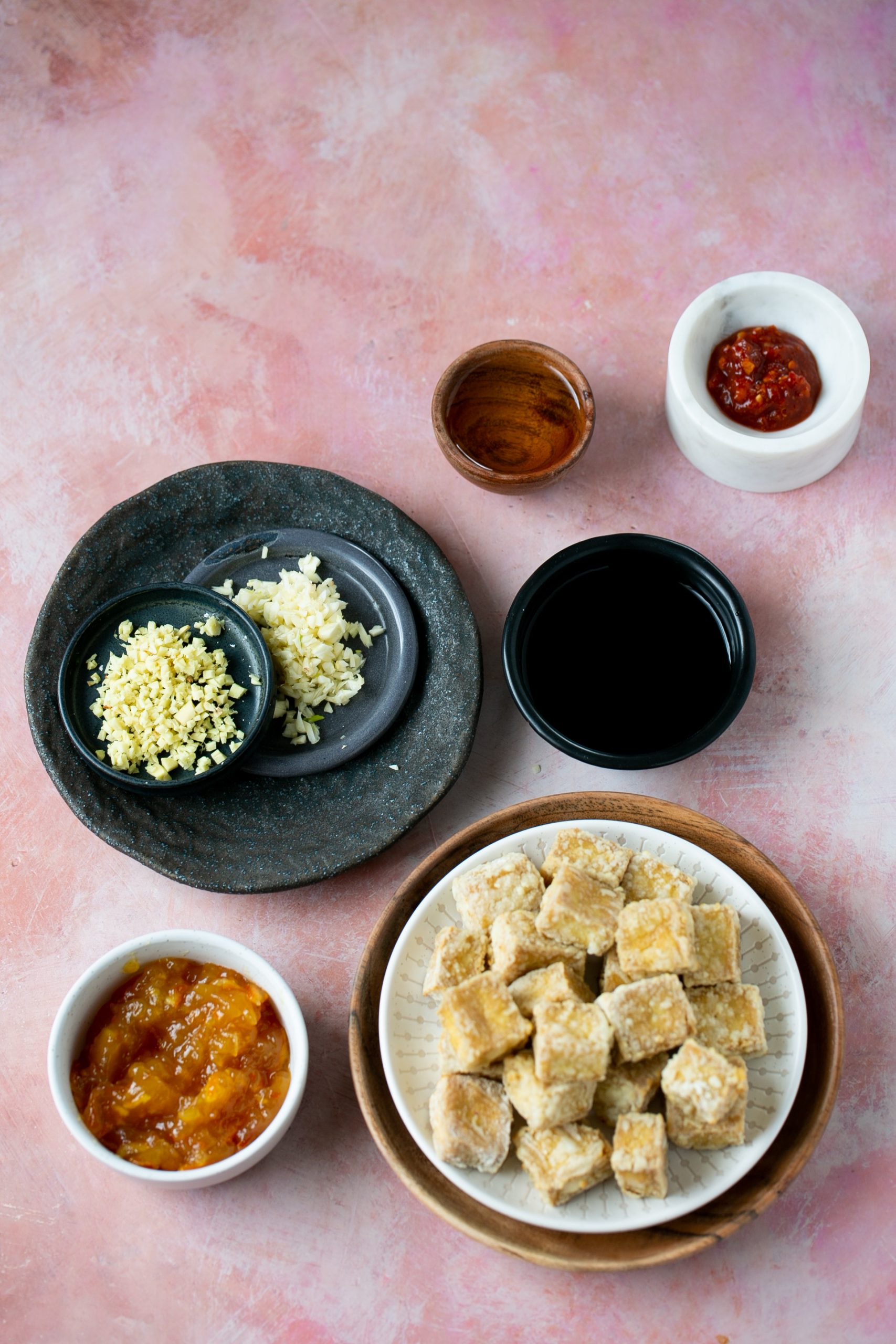         Descripción: Un plato de tofu crujiente sobre un fondo rosa con salsas picantes de naranja y condimentos.