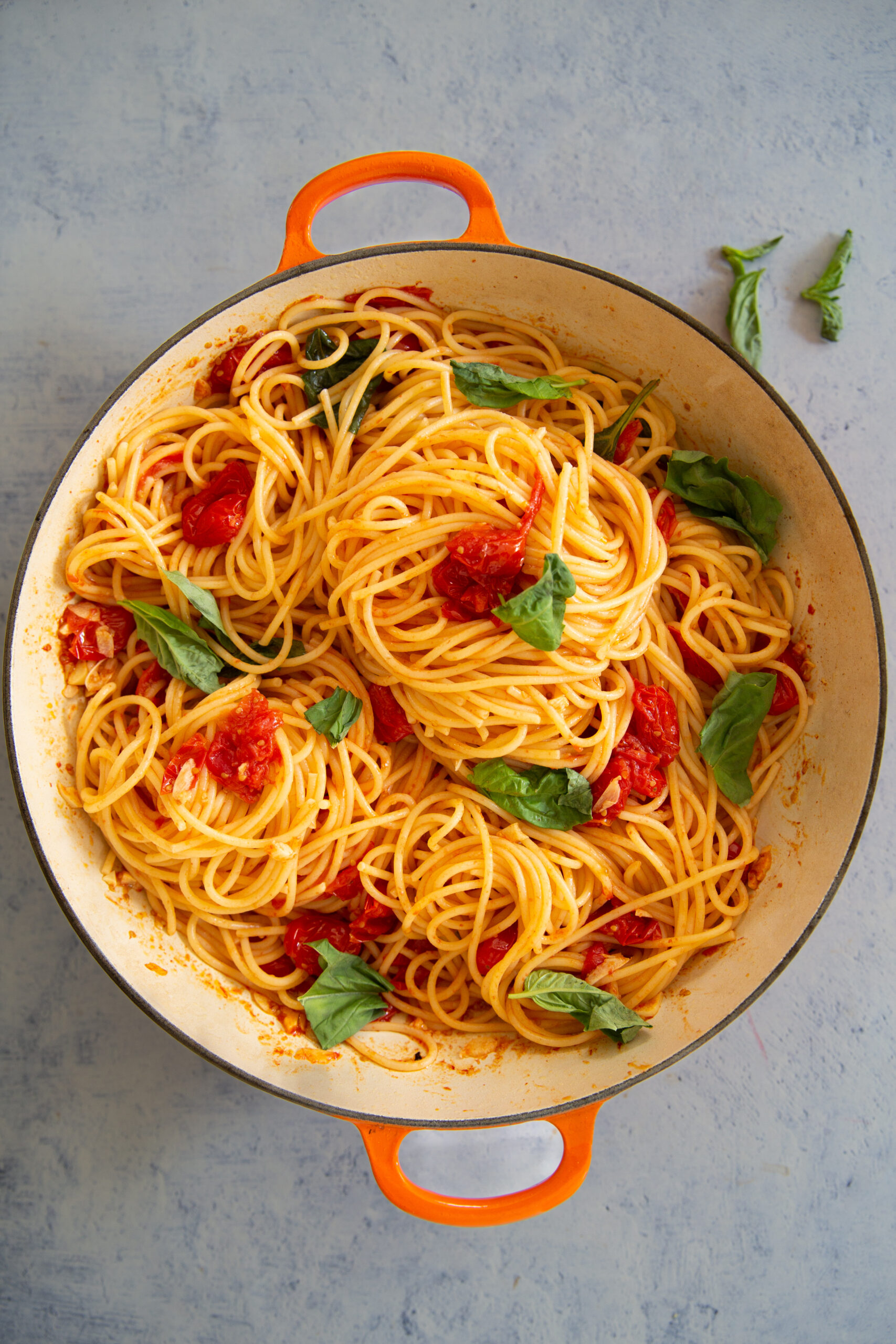 Pasta with cherry tomatoes and basil in an orange pot.