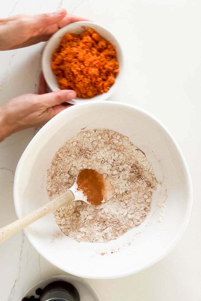 Flour and spices in a bowl with a plate with grated carrot on the side