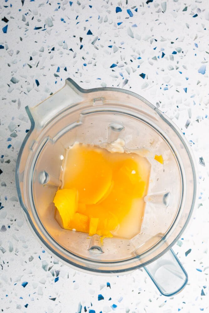 mango, agua, yogur en el vaso de la licuadora