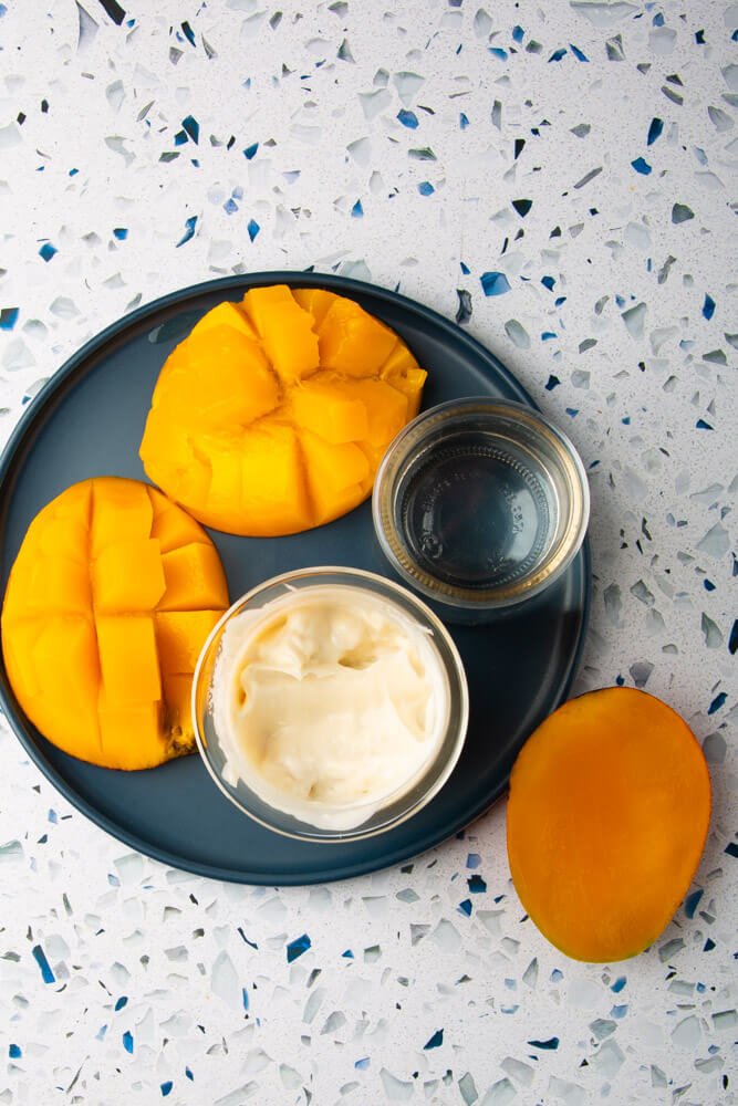 split mangoes, vegan yogurt and water on blue plate