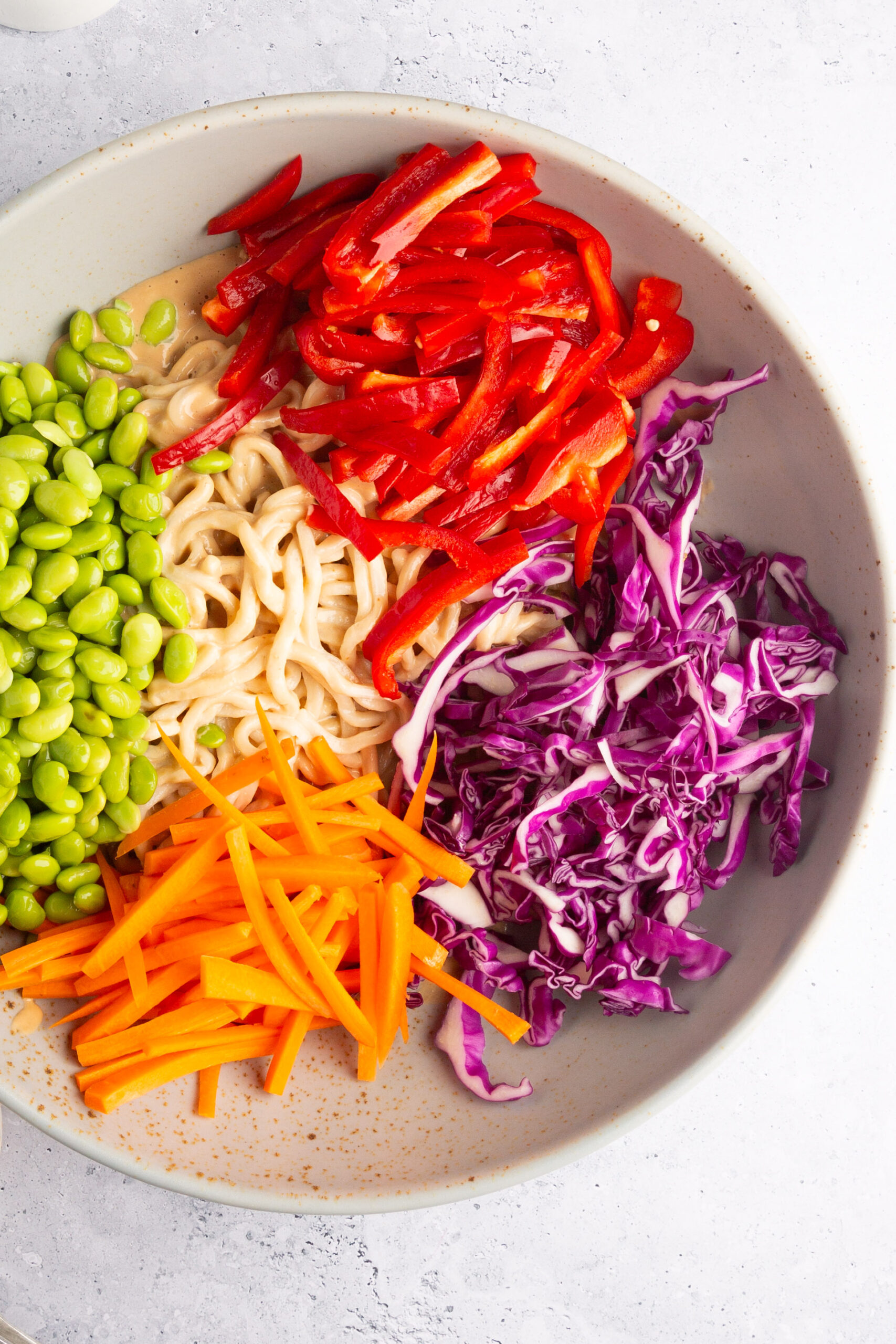 large bowl with noodles, with creamy dressing and red cabagge, edamame, red bell pepper and carrots
