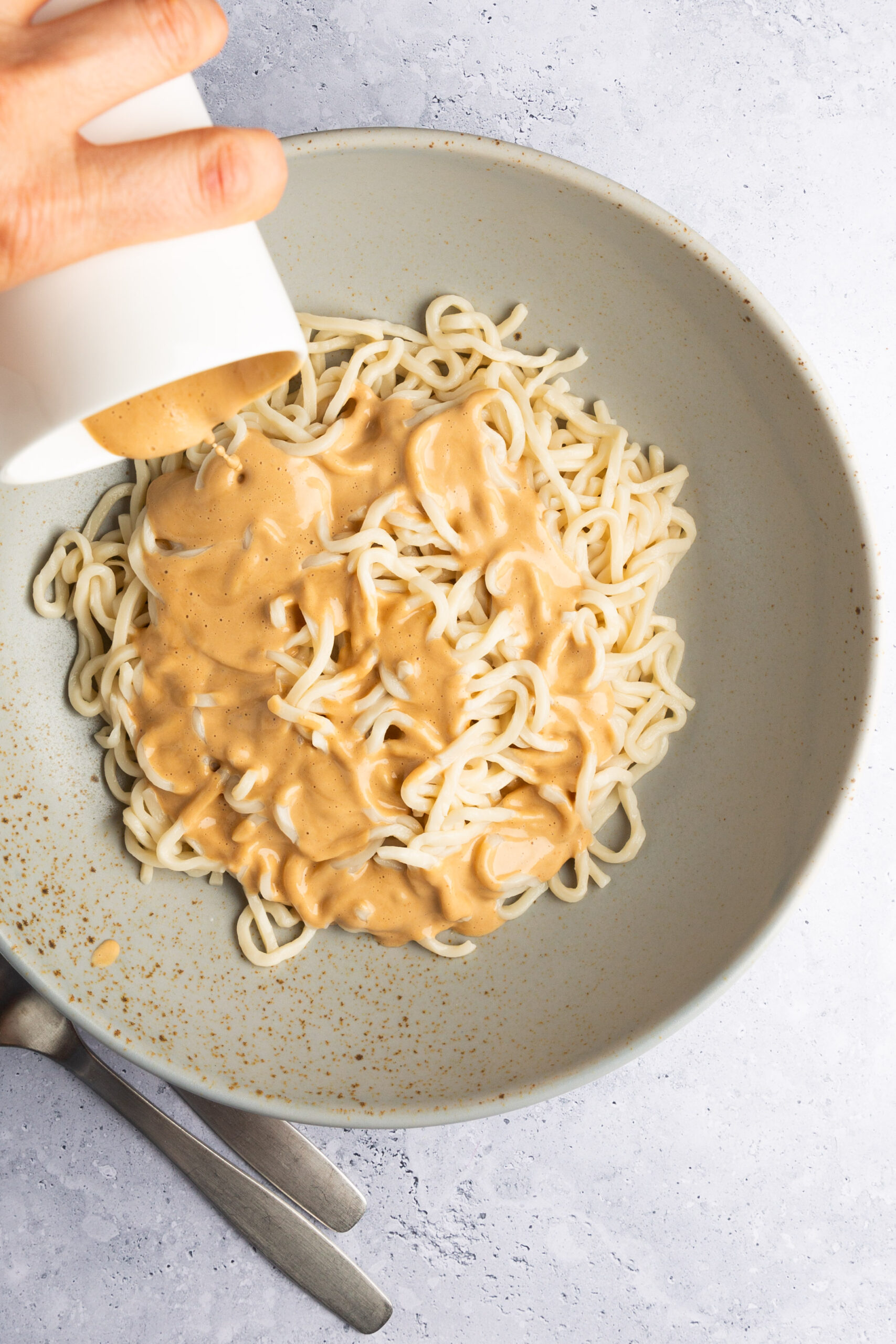 Pouring homemade spicy cashew dressing to a bowl with gluten-free noodles