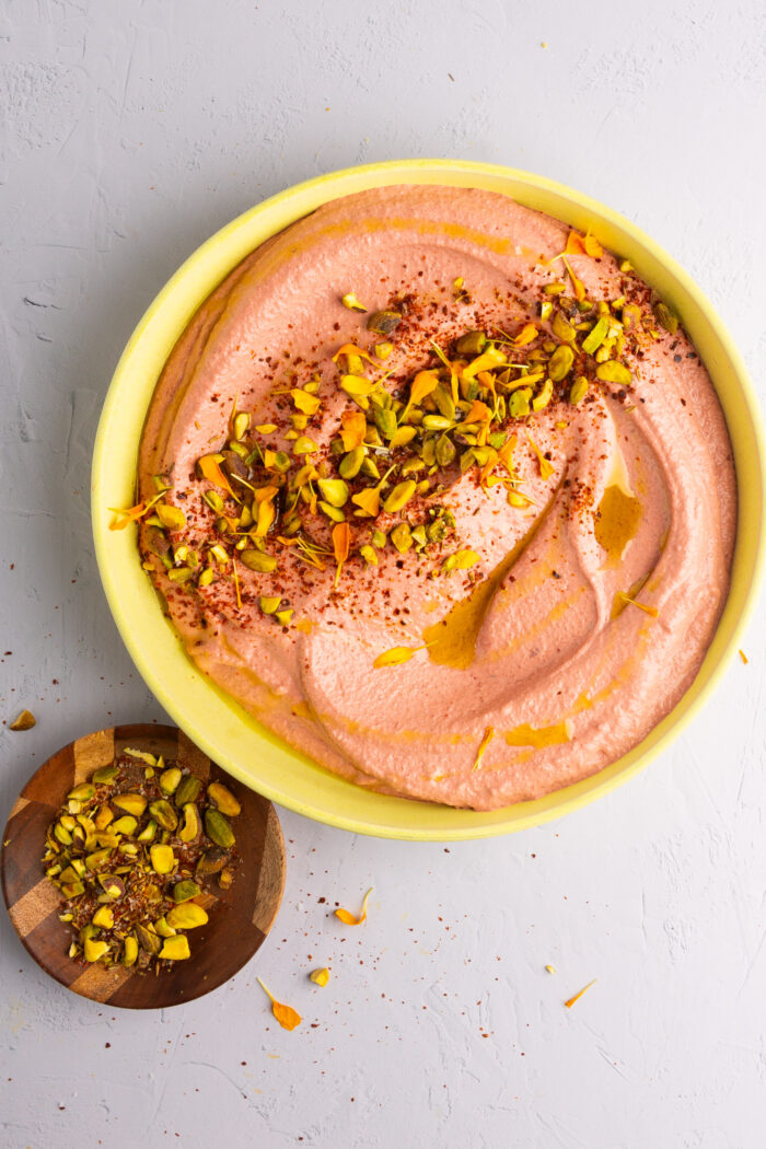 Hummus with beet on a yellow platter with flowers and pistachios on top