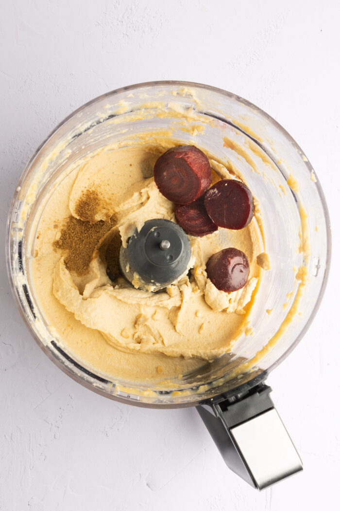 Hummus, beets and cumin in the bowl of a food processor.