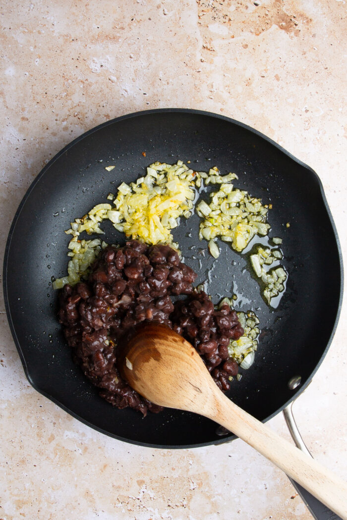 Black beans in a frying pan with a wooden spoon.