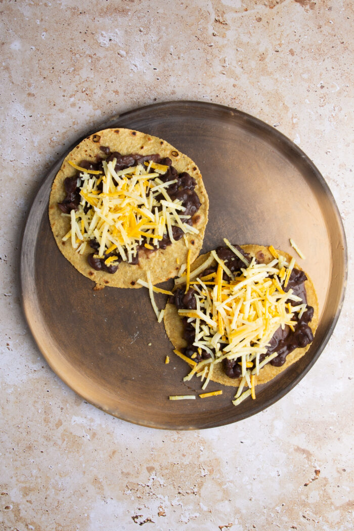 two corn tortillas with refried beans and vegan cheese on top