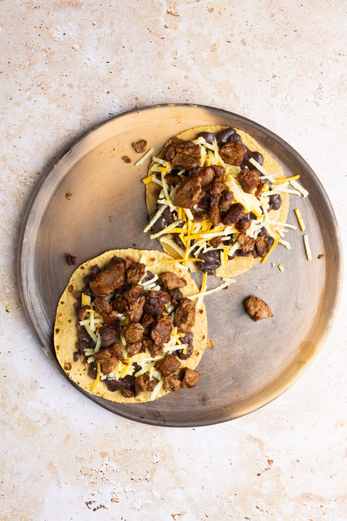 two crispy corn tortillas with beans, cheese and carne asada