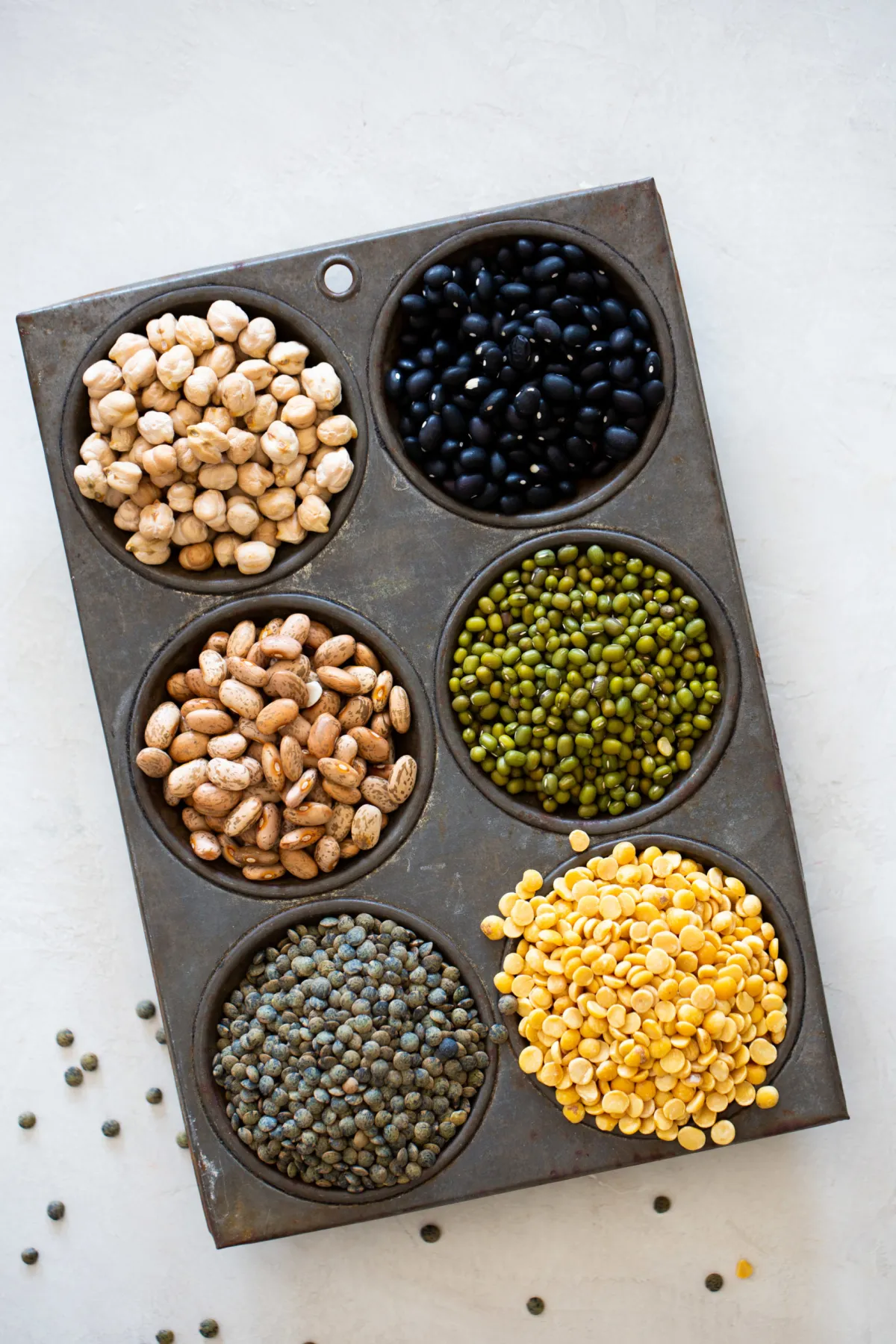 A metal pan filled with 25 essential vegan pantry ingredients including black beans, peas, and lentils.