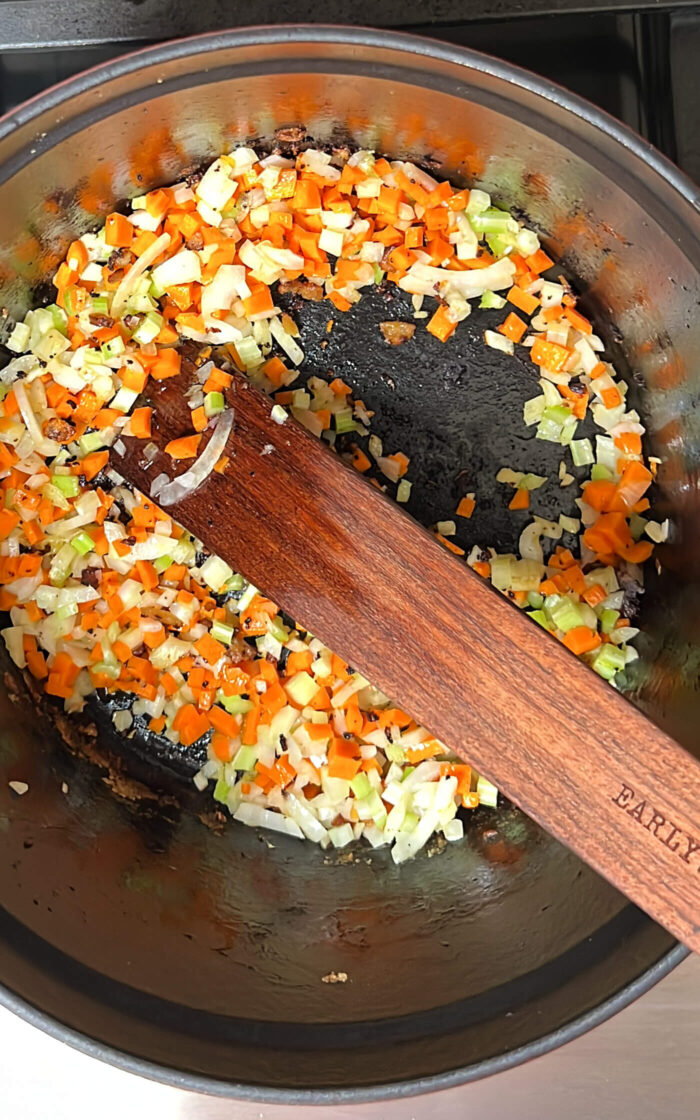 A wooden spatula is being used to stir up vegetables in a pan for a deliciously creamy vegan soup.