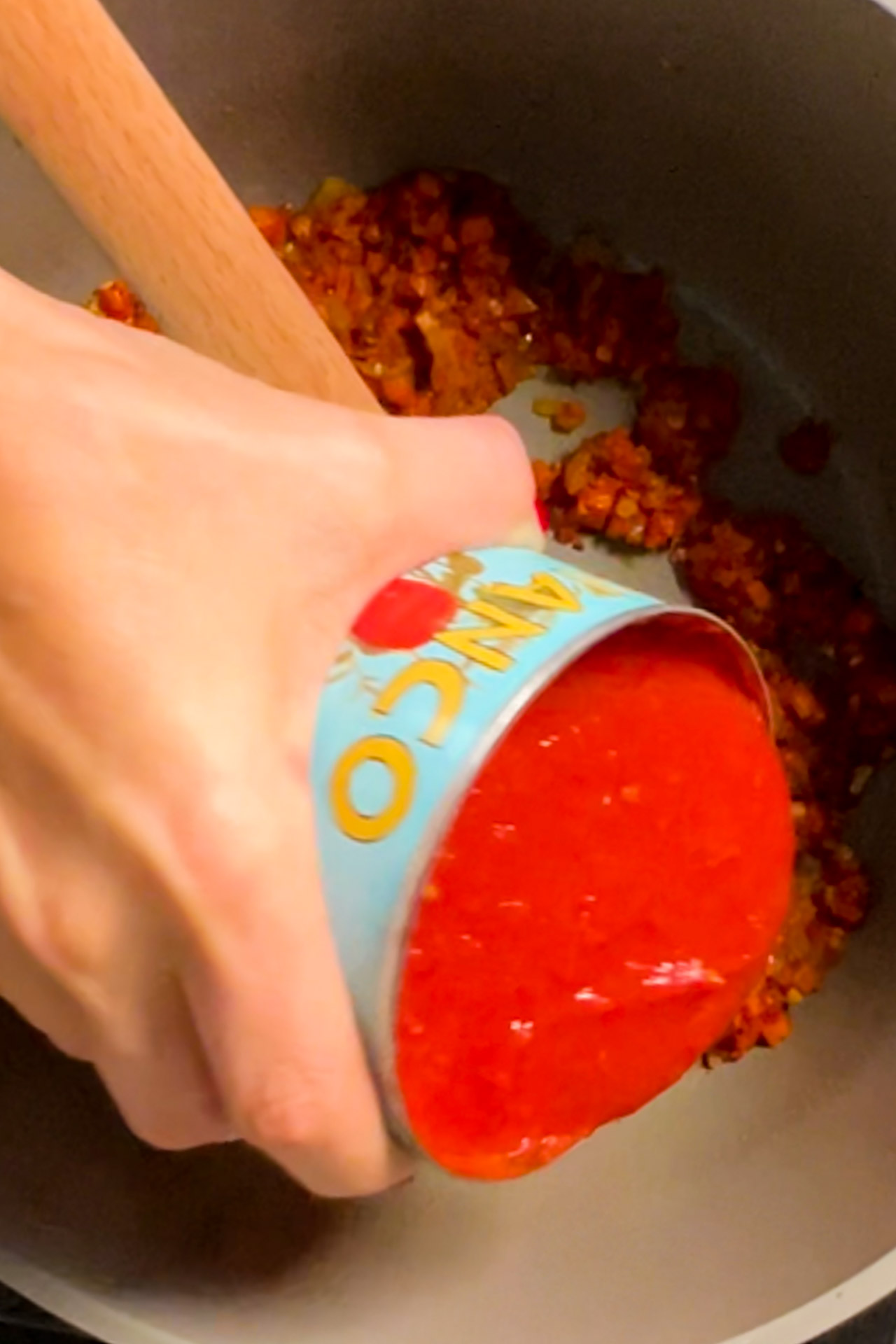 A vegan person pouring tomato sauce in a pan.