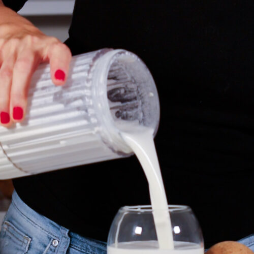 A woman pouring milk into a glass to make the best homemade vegan heavy cream.