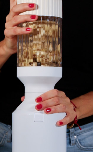 A woman is holding up a machine that is filled with nuts, experimenting with the best vegan heavy cream recipe.