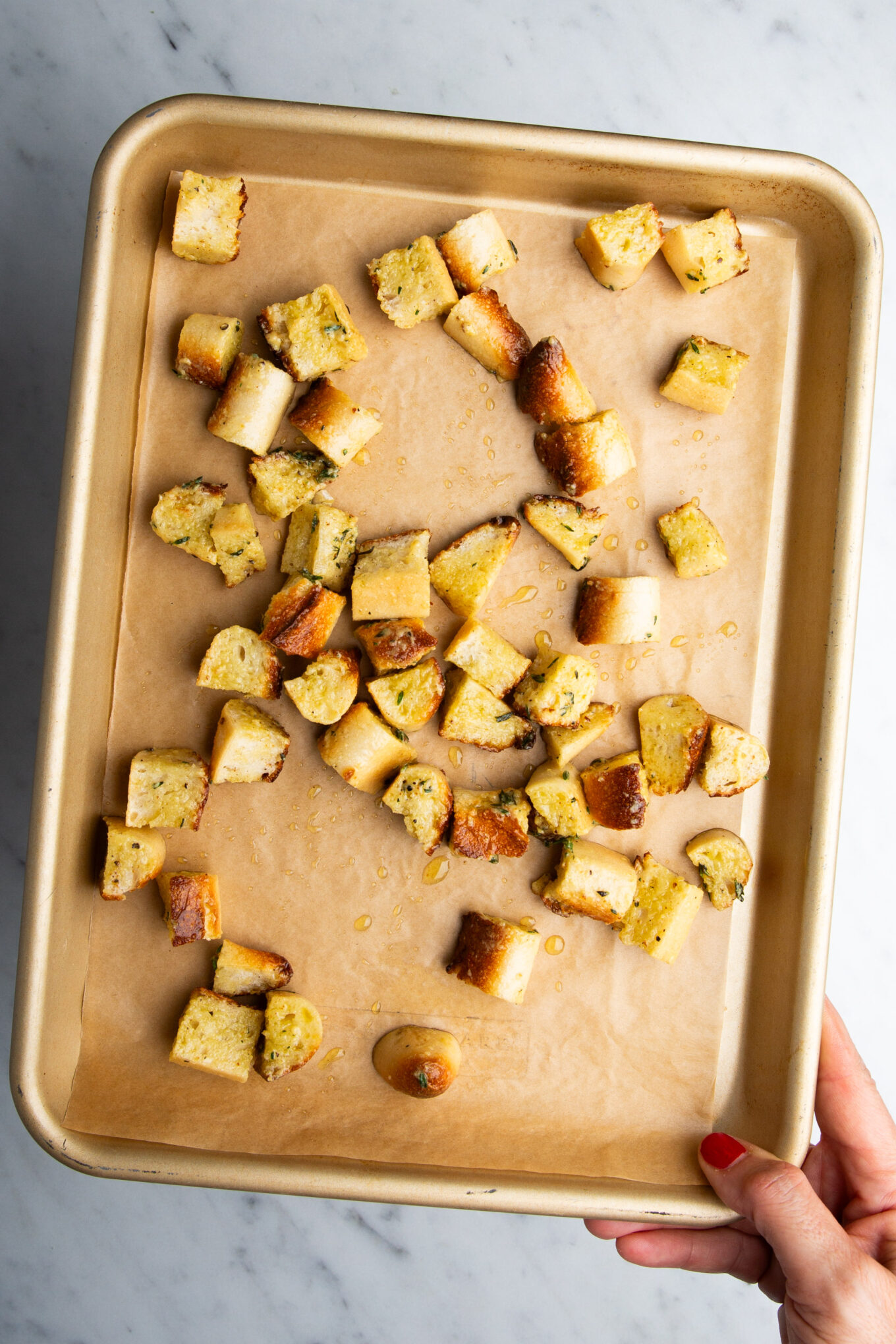 A person holding a baking sheet with croutons for cauliflower soup.