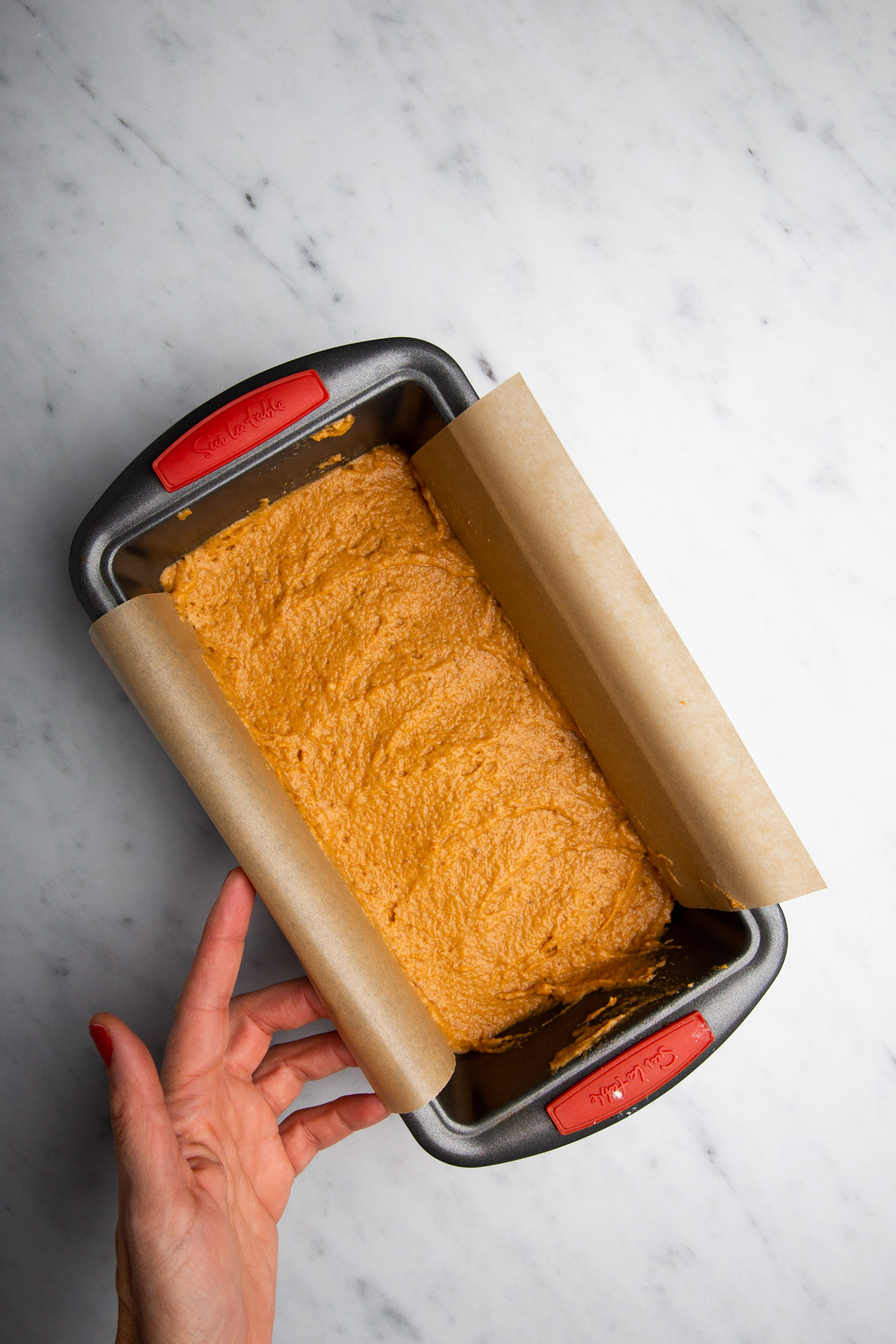 A person holding a baking pan with a piece of Vegan Spiced Pumpkin Bread in it.