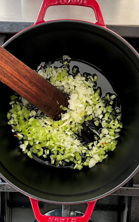 Sauteing onions in a pan with a wooden spoon to prepare a quick and healthy tortellini soup.