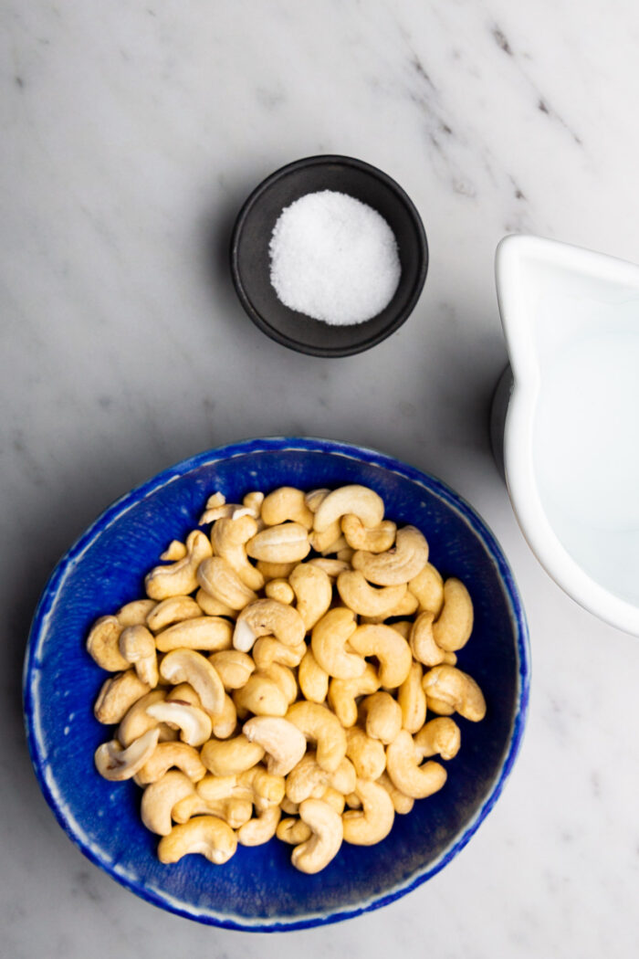 Cashews in a bowl next to a bowl of salt, a perfect combination for making creamy vegan recipes.