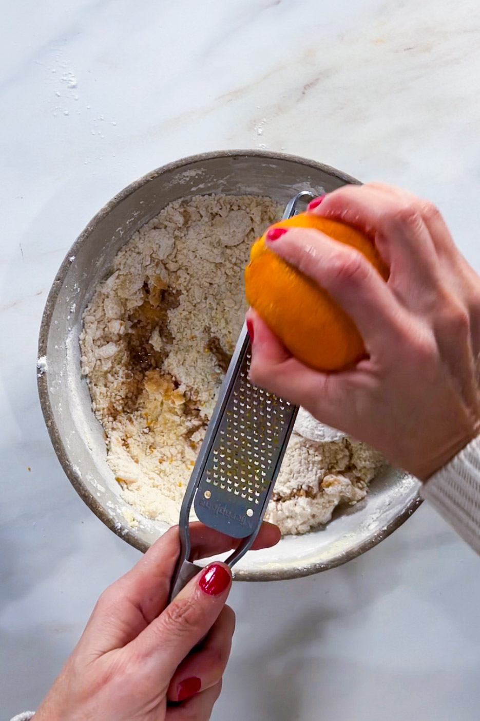 A person grating an orange into a bowl of flour to make Day of the Dead cookies.