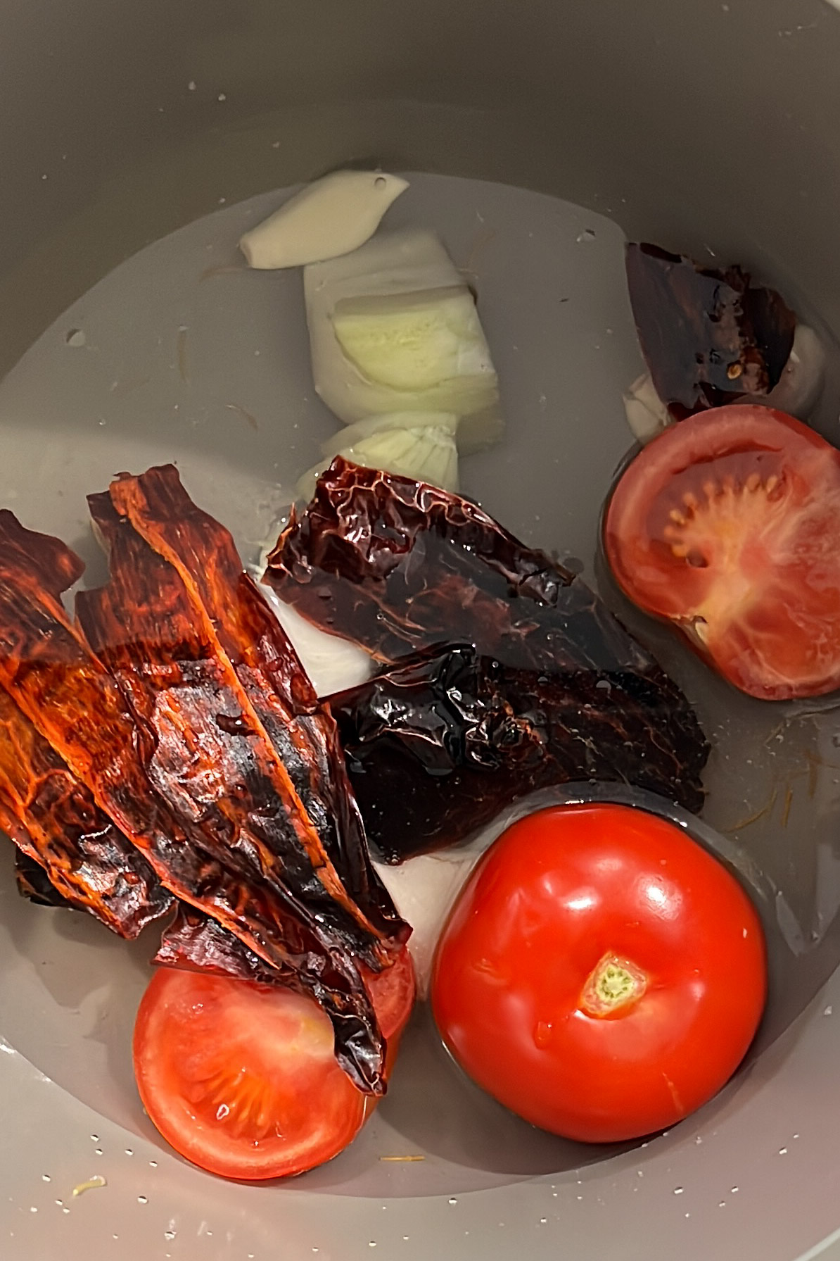 Una olla con tomates, cebollas y pimientos hirviendo a fuego lento para crear una sabrosa Sopa de Fideo.