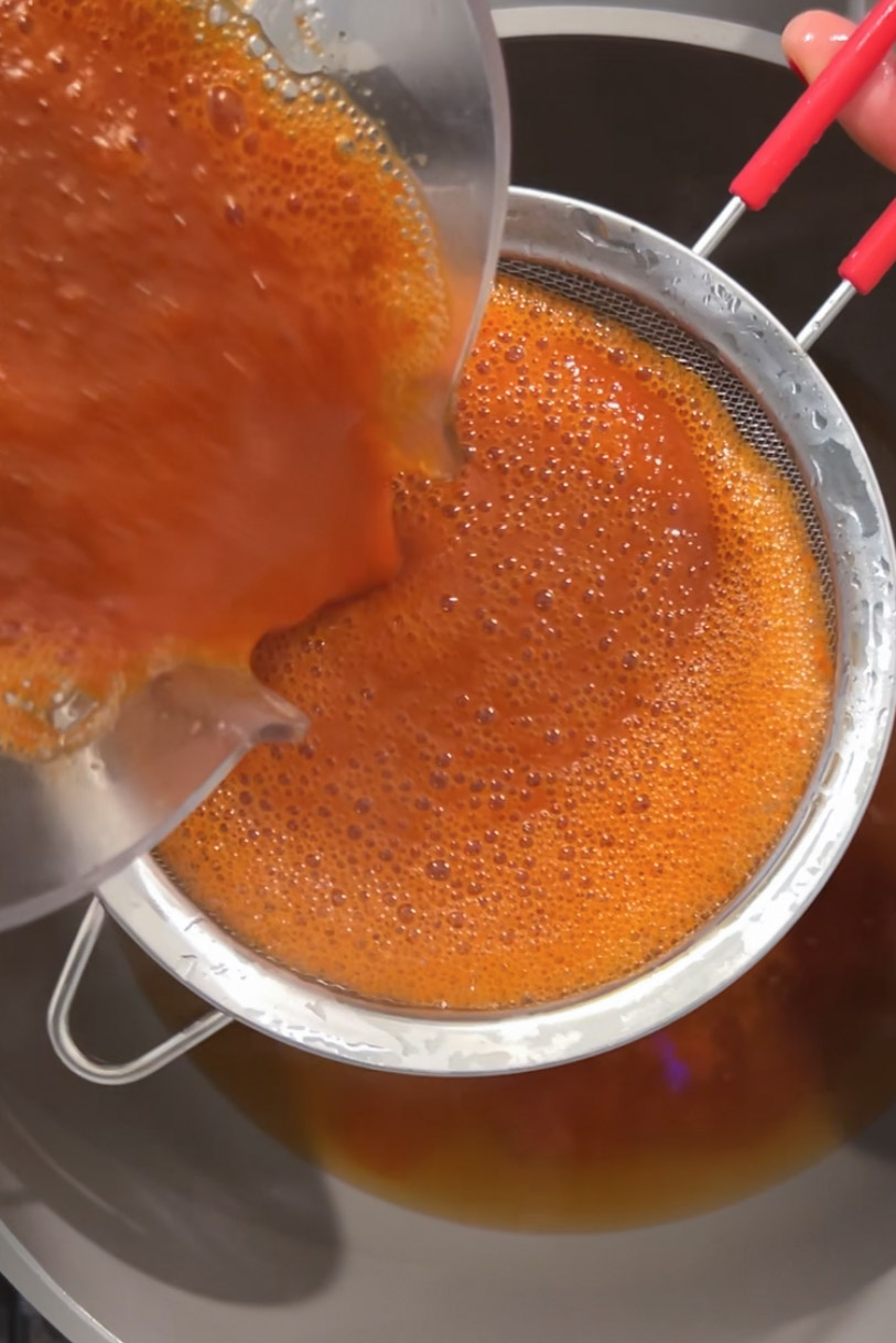 A person pouring Sopa de Fideo into a pan.