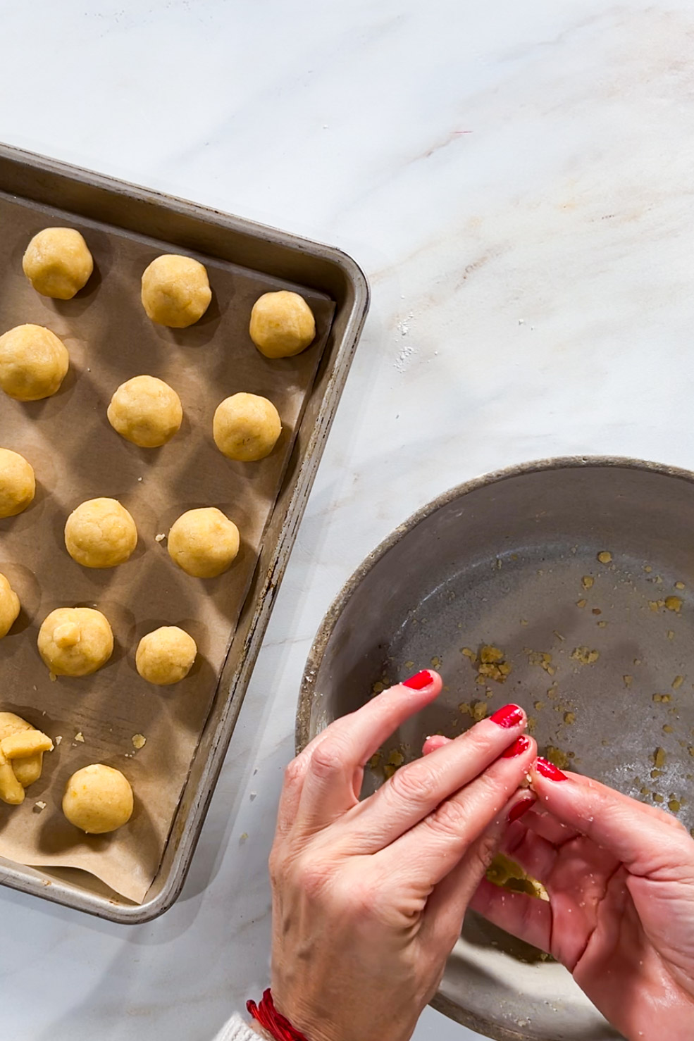 A person is putting cookie dough balls into a pan.