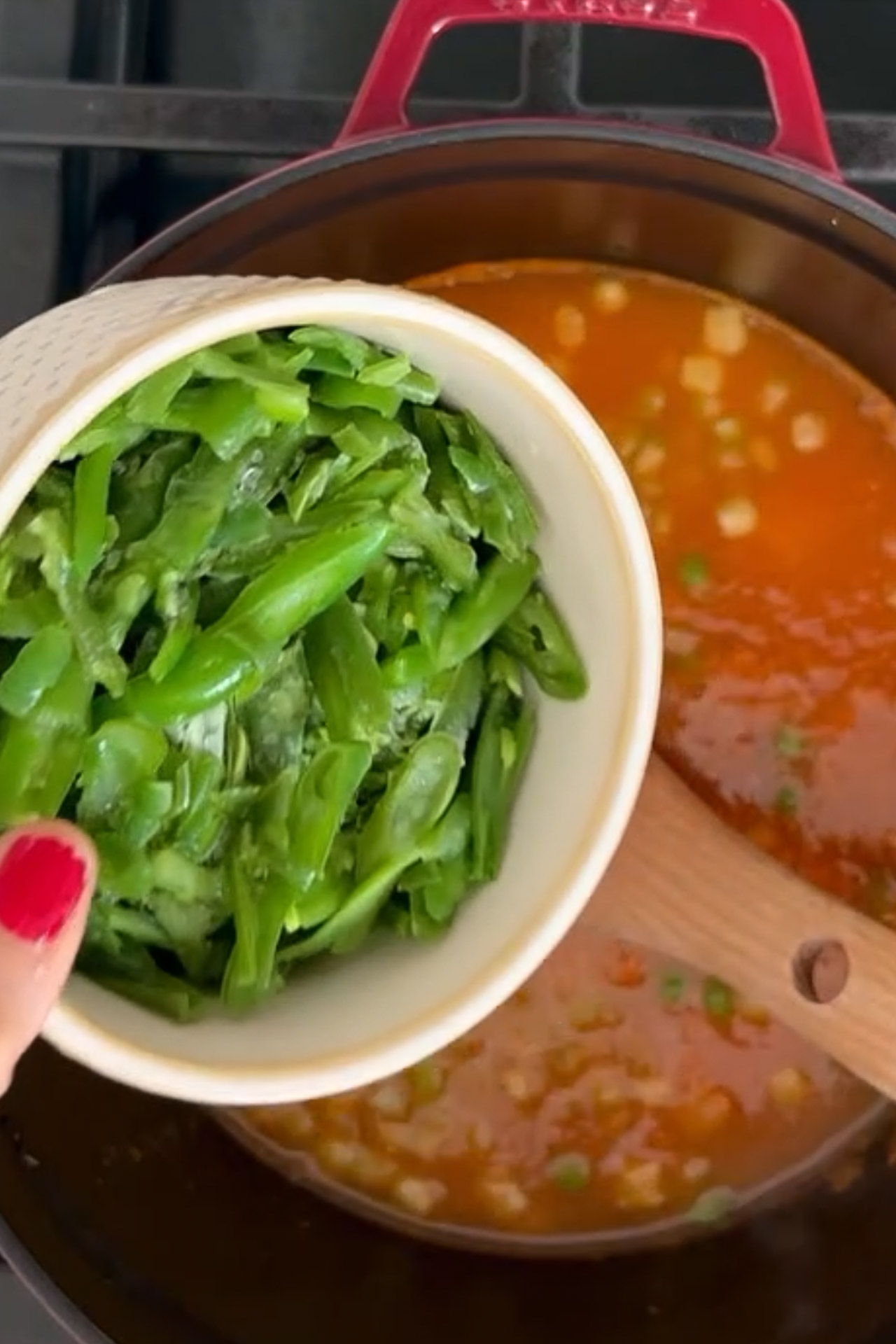 A person is stirring green beans into a pot of healthy soup.