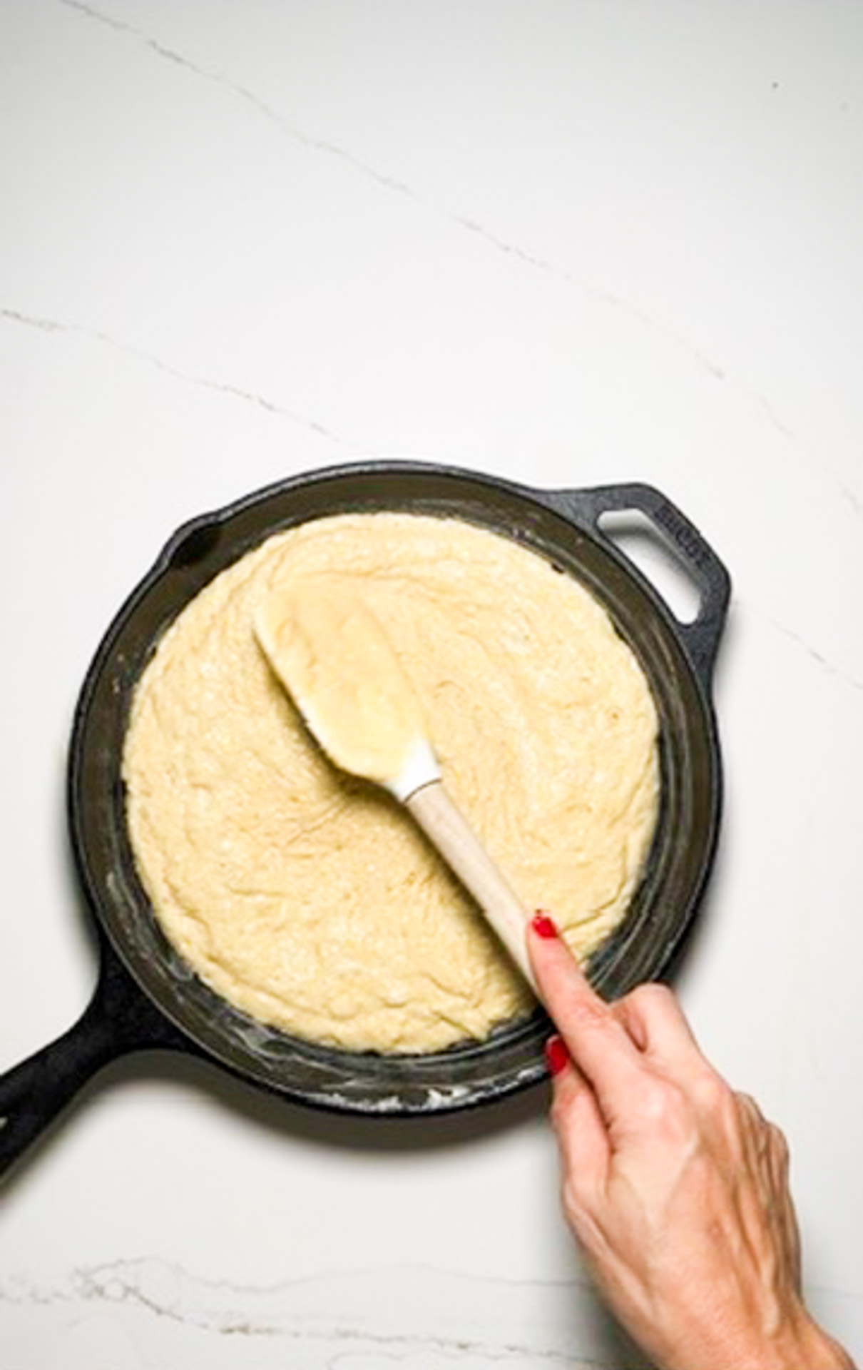 A vegan person using a spatula to stir a batter for a cornbread recipe in a skillet.