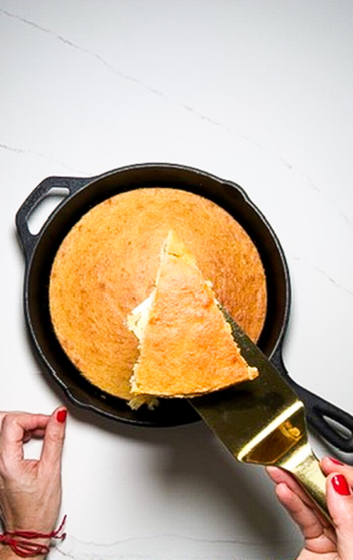 A person cutting a delicious piece of cornbread out of a skillet.