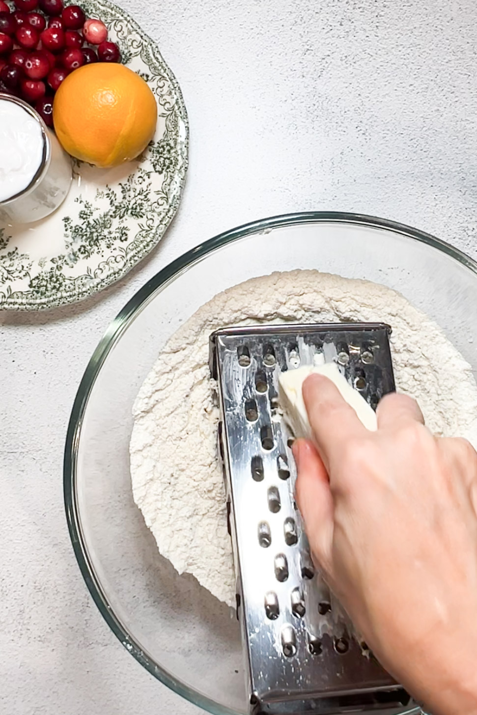 A vegan person using a grater to grate orange and cranberry dough.