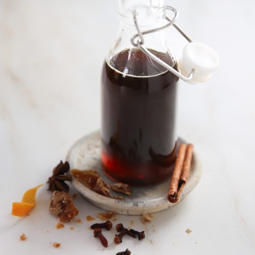 A glass bottle with cinnamon sticks and spices infused coffee syrup on a white plate.