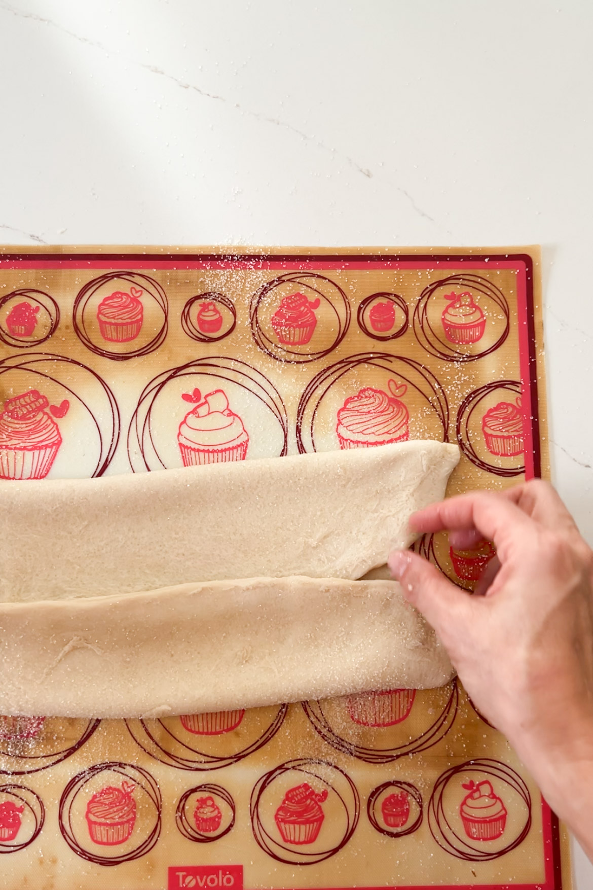 A person cutting a piece of Pan Dulce dough on a baking mat.
