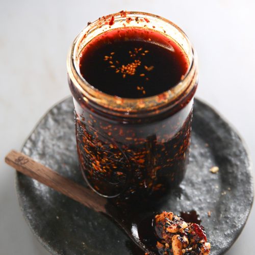 A jar of salsa macha sauce with a spoon on a plate.