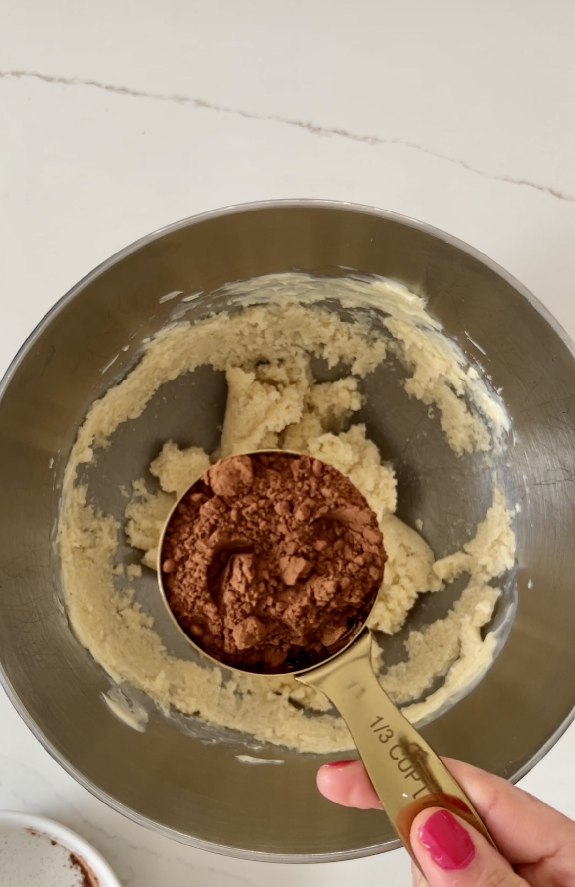 A vegan person is scooping double chocolate into a mixing bowl, preparing it for cookies.