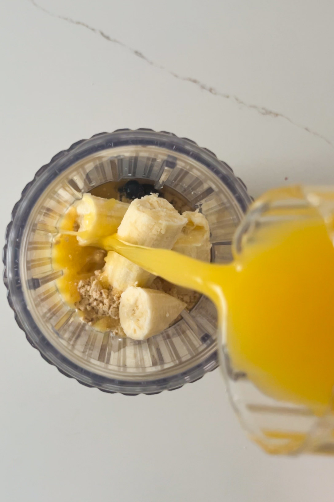 A smoothie is poured into a bowl with oatmeal and bananas.