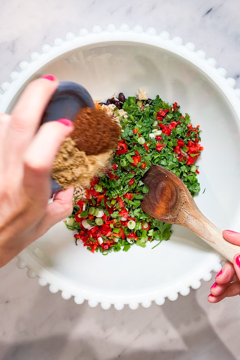 A person sprinkling southwestern spices on a plate of vegetables.