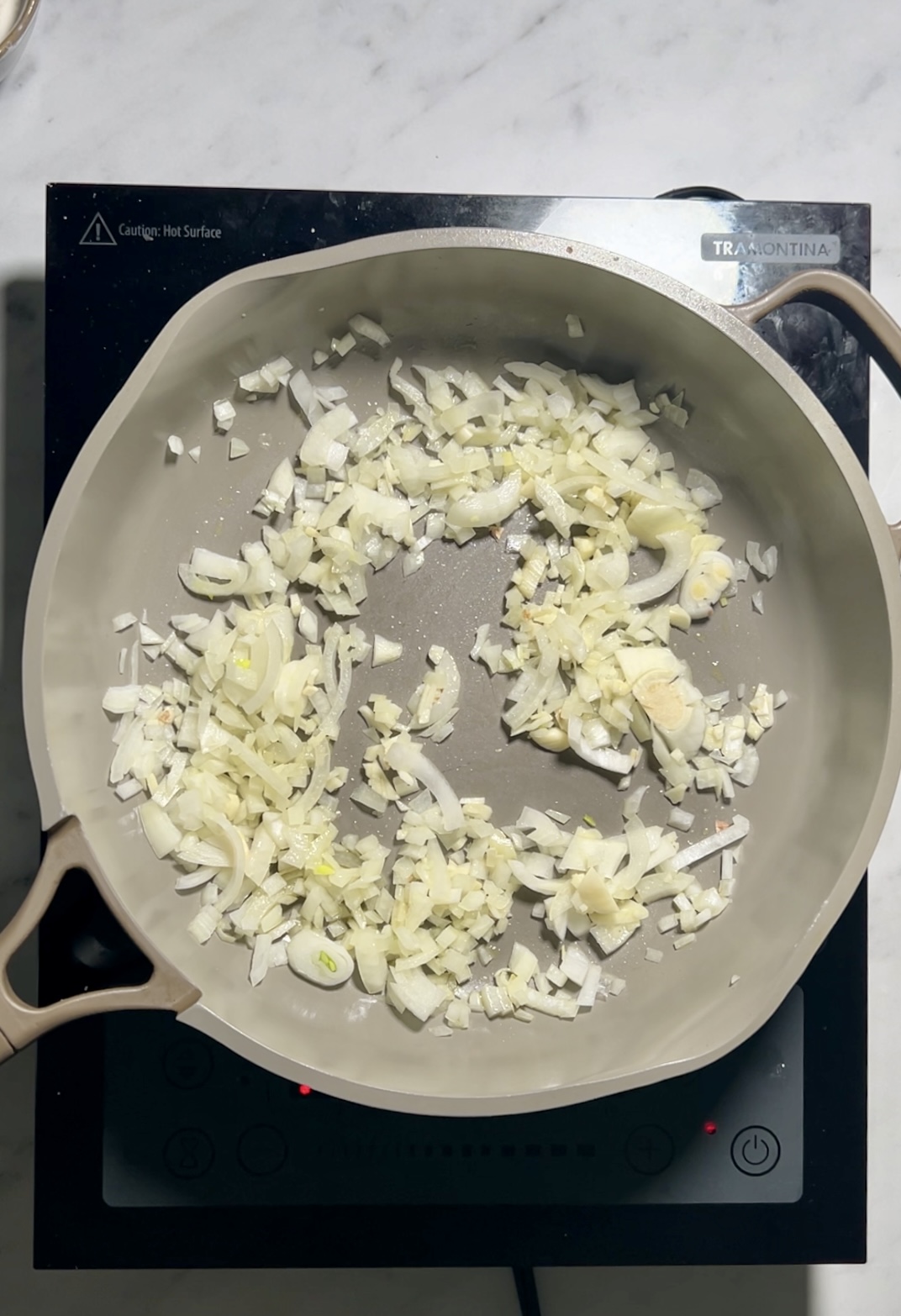Cebollas en rodajas chisporroteando en una sartén encima de la estufa.