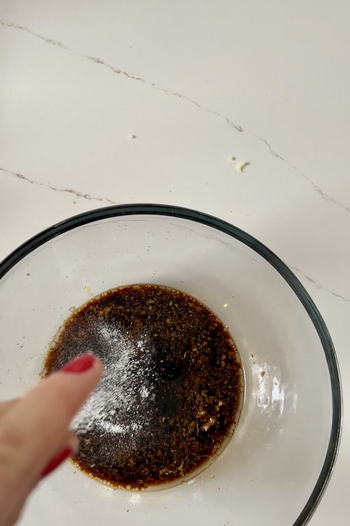 A person sprinkling brown sugar into a bowl while preparing stir-fry noodles.