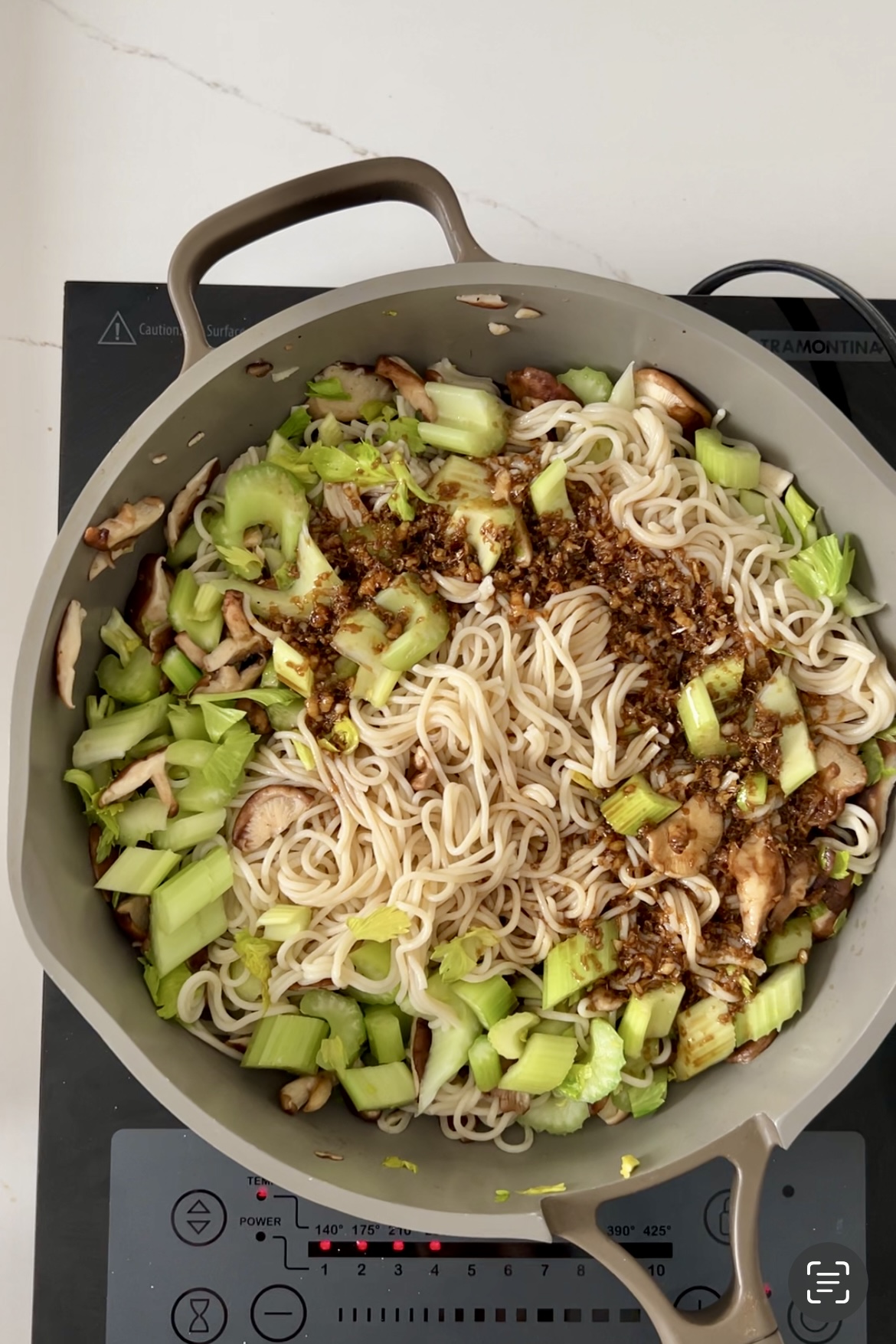 A pan full of stir-fry noodles and vegetables on top of a stove, sprinkled with black pepper.