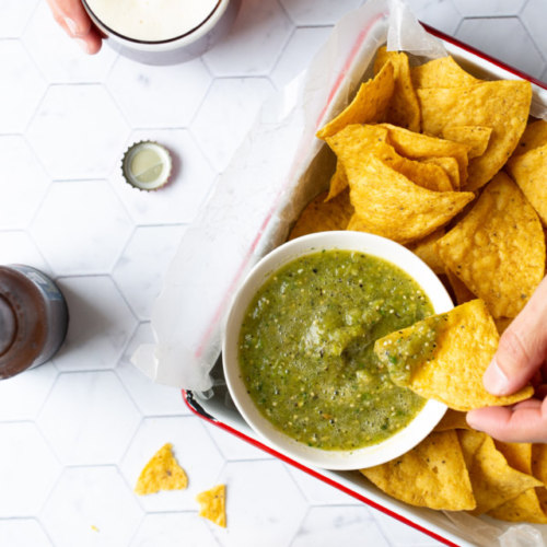 A person is dipping tortilla chips into a bowl of guacamole.