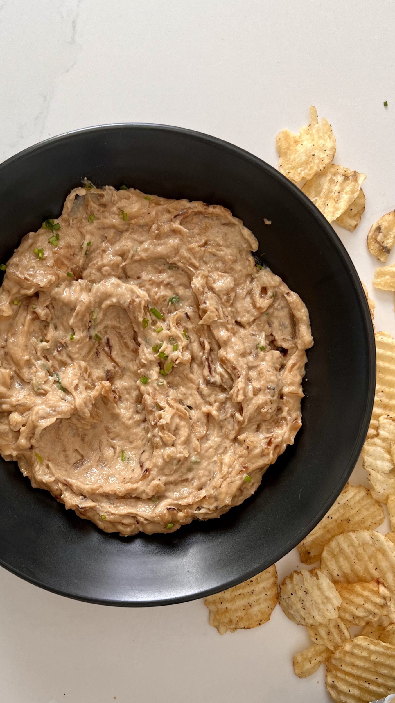 A plate of vegan onion dip with chips on the side.