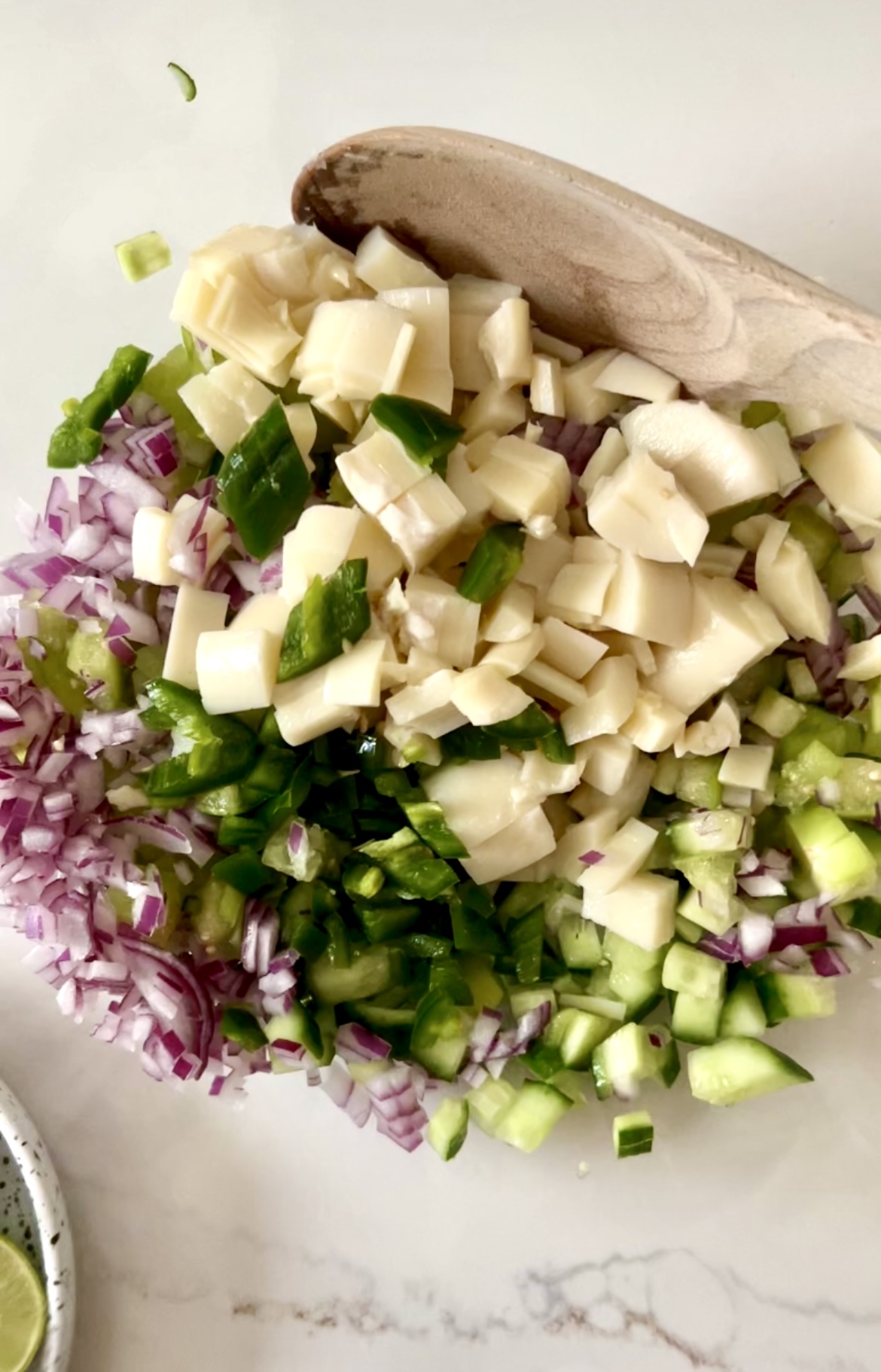A bowl of onions and green peppers chopped with a wooden spoon, perfect for making Ceviche verde.