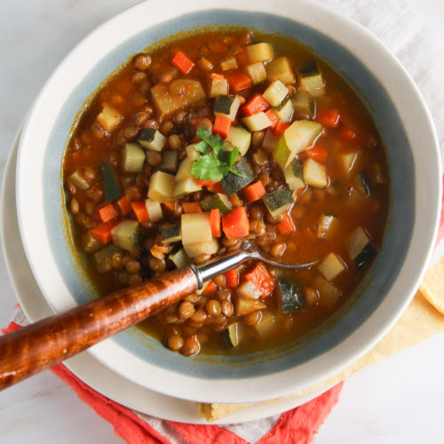 A bowl of lentil soup with vegetables and a spoon.