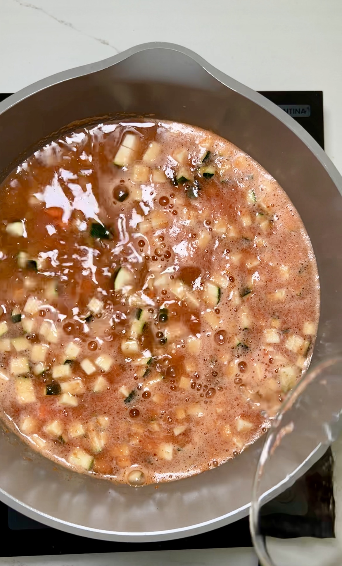 Una sartén llena de sopa de lentejas hirviendo a fuego lento sobre una estufa, repleta de sabrosos chiles chipotles y una variedad de vegetales frescos.