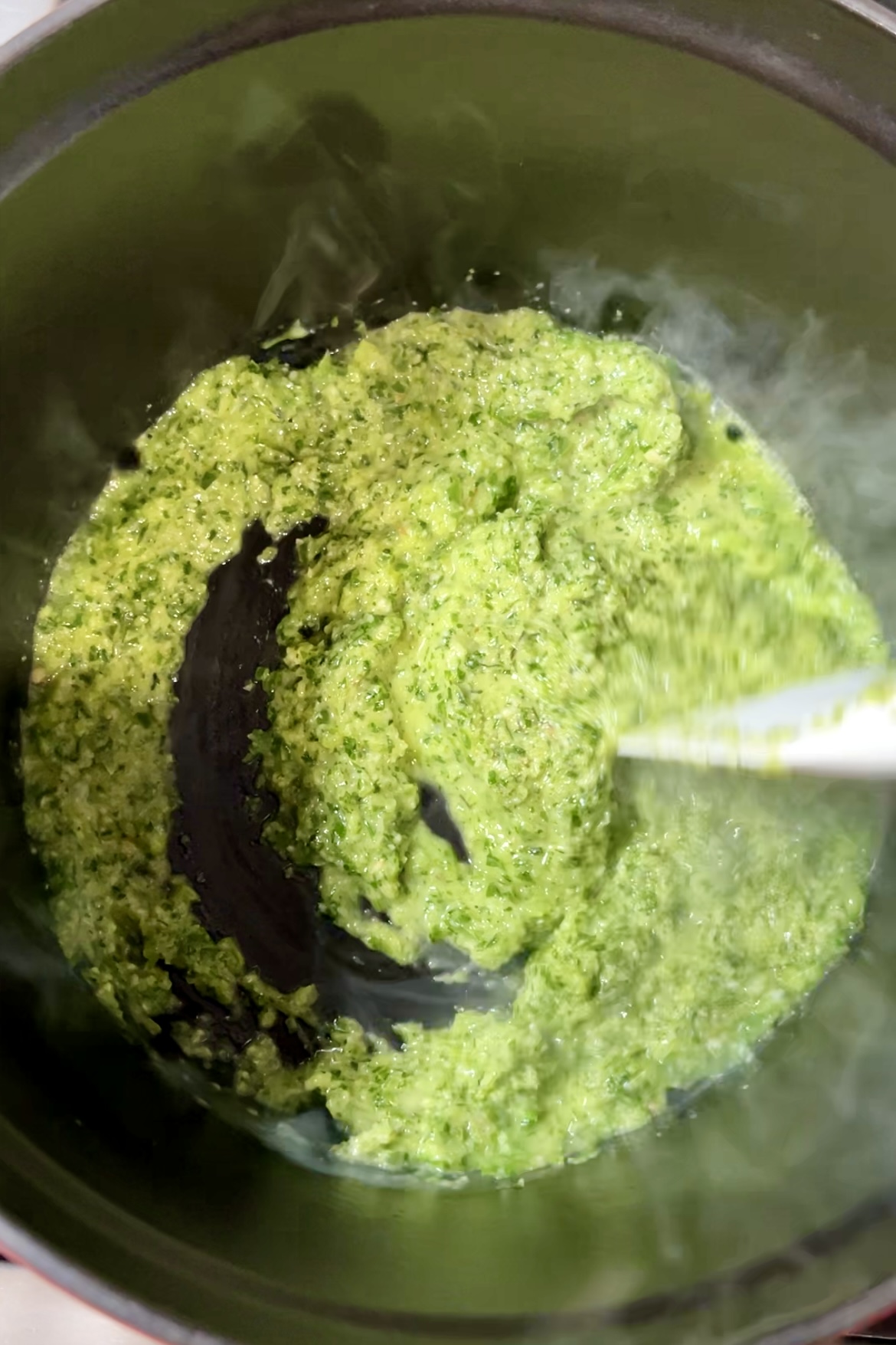 A green cilantro sauce that is stirred in a pot.