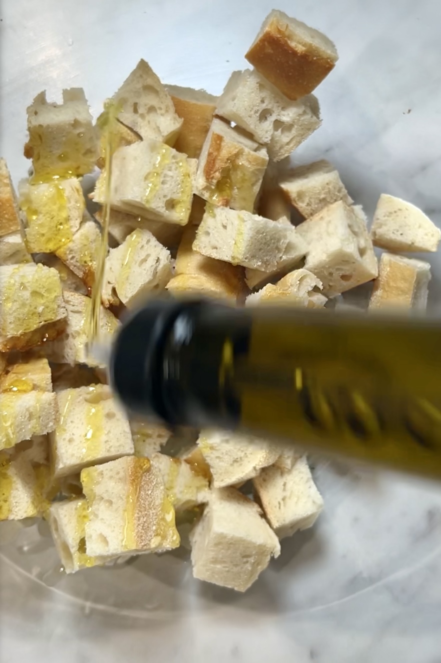 A bottle of olive oil is poured on a plate of croutons with Bread and Garlic.