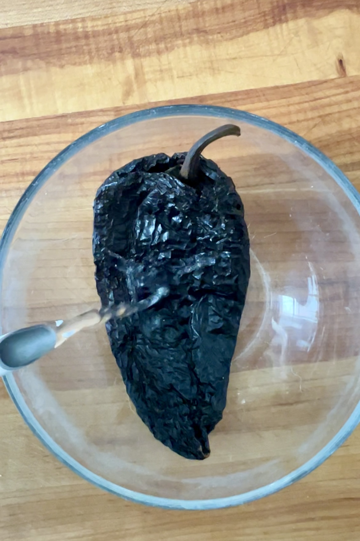 One ancho chile in a glass bowl with a spoon.