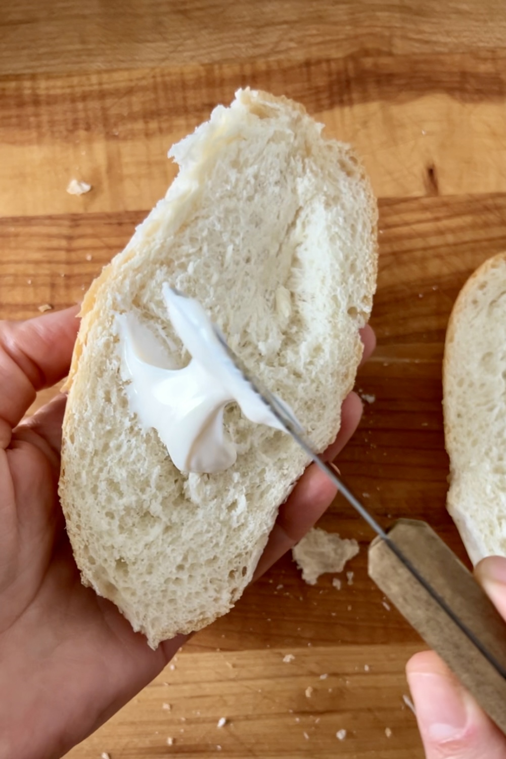 A person cutting a piece of bread with a knife to prepare spicy sandwiches.